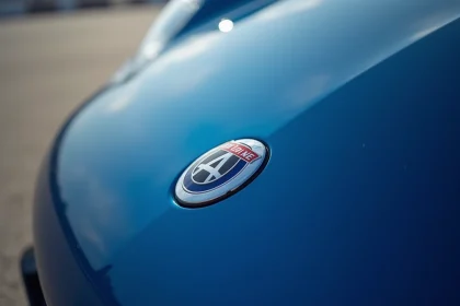 Gros plan hyperréaliste du logo Alpine sur le capot d'une voiture de sport bleue, emblème chromé avec relief détaillé